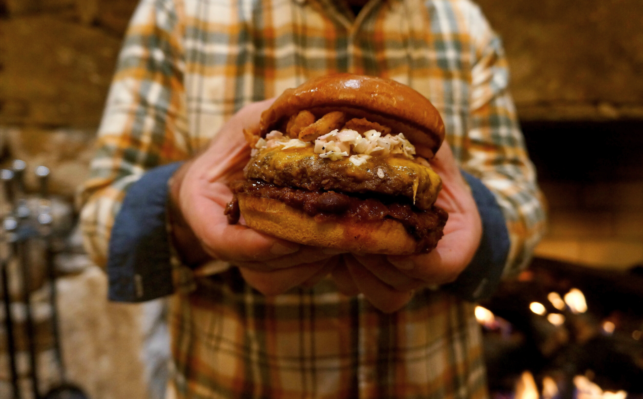 A man holds out The Red Fox restaurant's hearty "The Carolina Burger" toward the camera.
